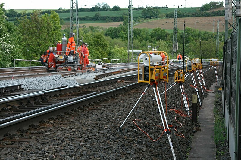 Gleisbaustelle mit Bautrupp links und Warngeberkette rechts am Gleis